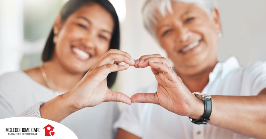 A daughter and an older mother create a heart with their hands, representing the feeling that is highlighted during National Family Caregivers Month