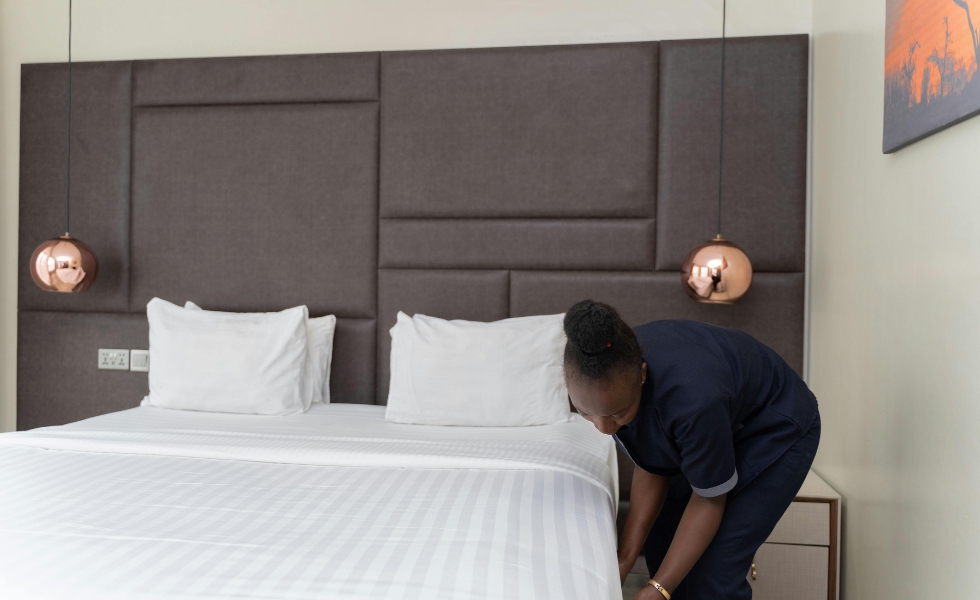 A woman care giver tucks a bed sheet under a bed in a bedroom. Light Housekeeping in Columbia