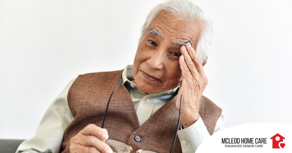 An older adult holds his head and his glasses representing vision problems like macular degeneration.