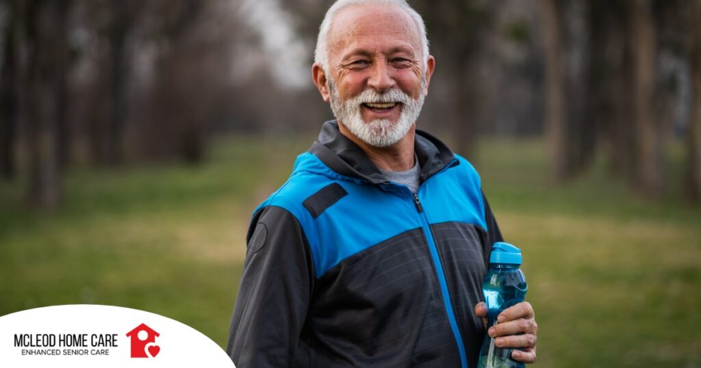 An older man smiles with a water bottle while exercising, representing the benefits of encouraging exercise when caring for seniors at home.