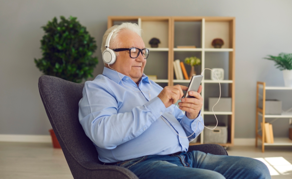 Tech Savvy Senior A Tech Savvy Senior in Columbia is seated comfortably in a modern living room, wearing headphones and smiling while using a smartphone, enjoying technology with ease.