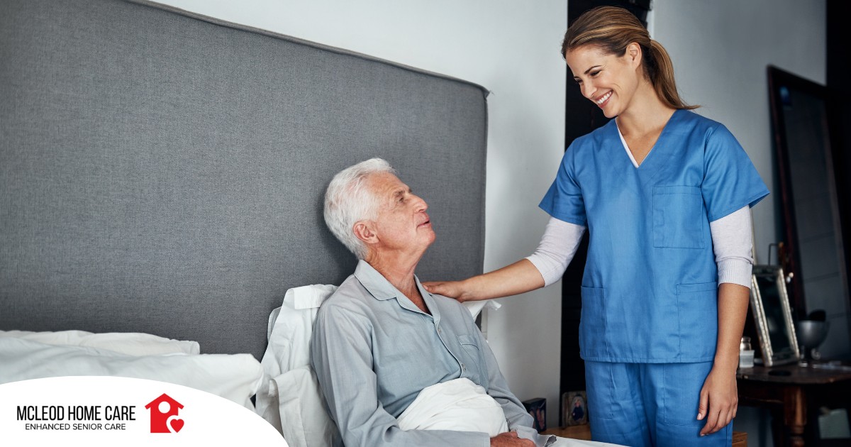 A caregiver smiles at an older client in bed, representing the compassion involved in being a live-in caregiver.