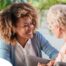 A caregiver smiles at an older client in a chair, representing the joy that can come from a healthy work-life balance.