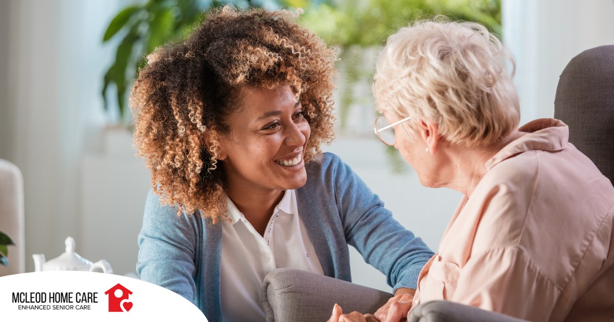 A caregiver smiles at an older client in a chair, representing the joy that can come from a healthy work-life balance.