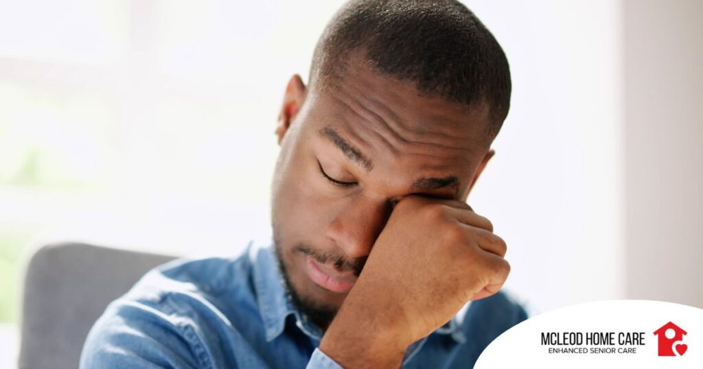 A man tiredly rubs his eyes, representing the exhaustion that can come with family caregiving.